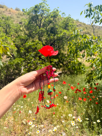 Mano sosteniendo el Collar Florero con amapola roja en el jarrón de porcelana – joya esdeinés